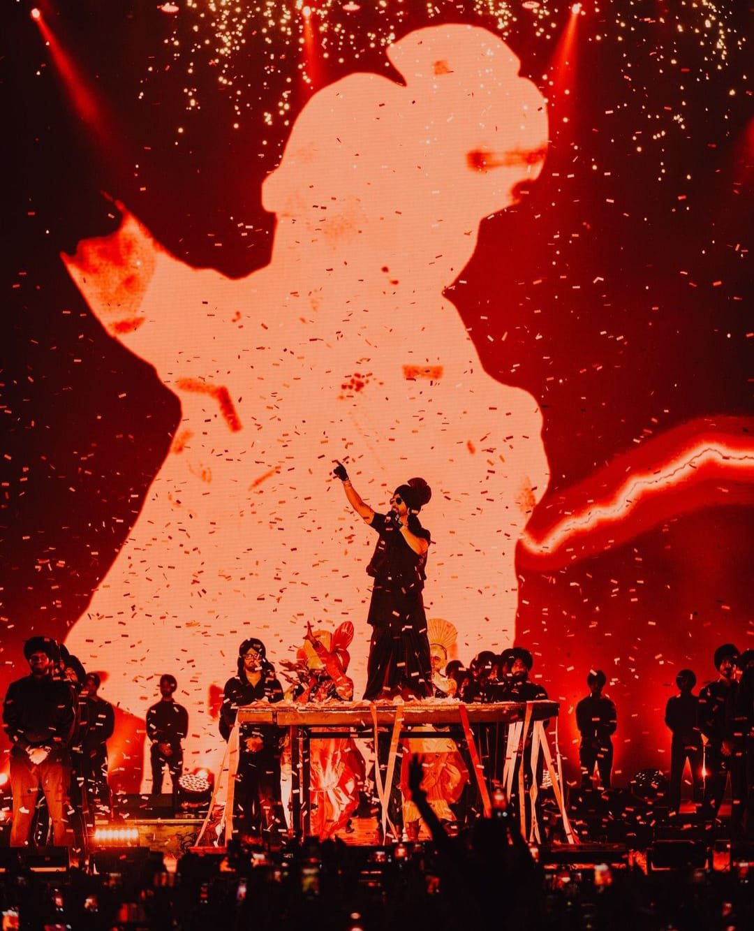 Performer silhouetted against red light and confetti on the Dil-Luminati Tour