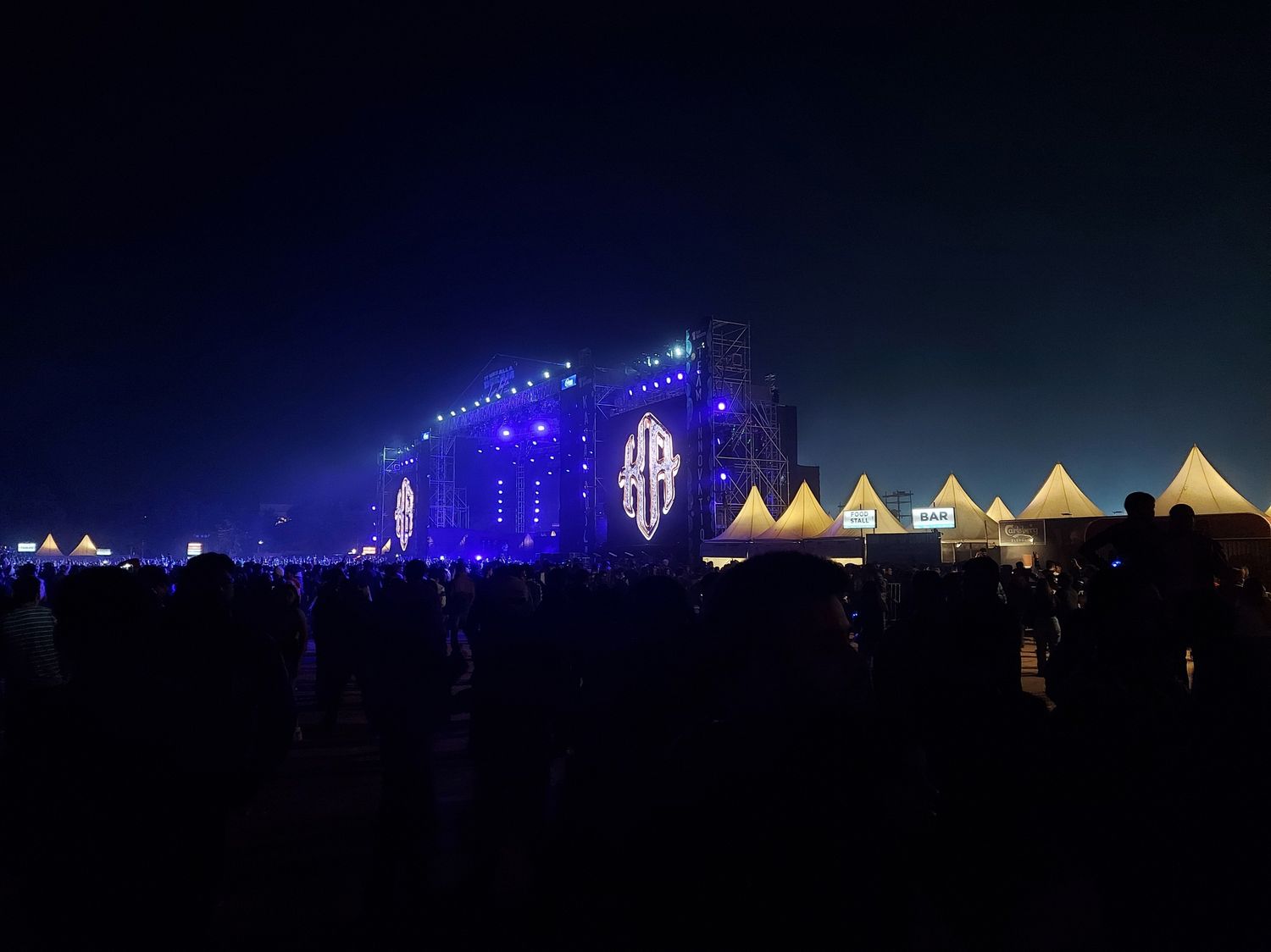 Wide night view of a large outdoor concert stage lit for a Karan Aujla live show
