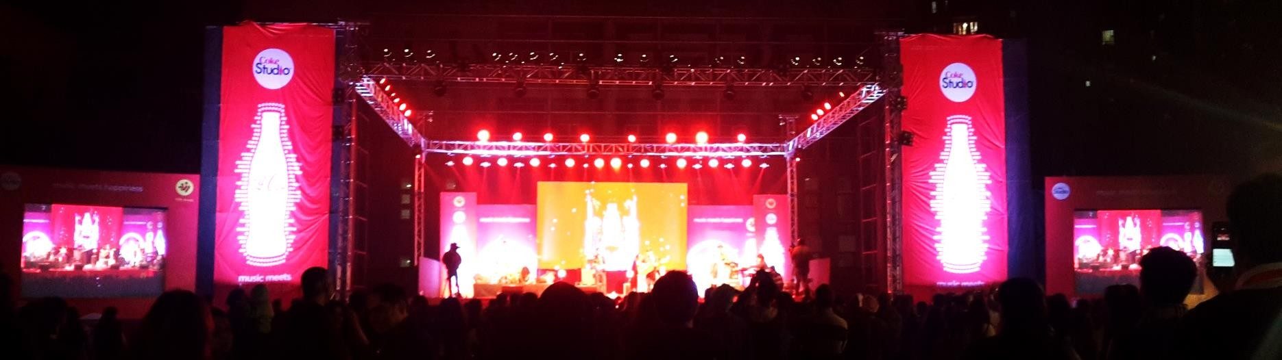 Panoramic red-lit concert stage flanked by tall sound and light towers