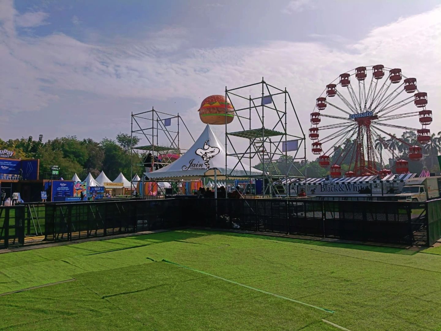 Daytime festival ground with a ferris wheel and stage builds at Zomaland
