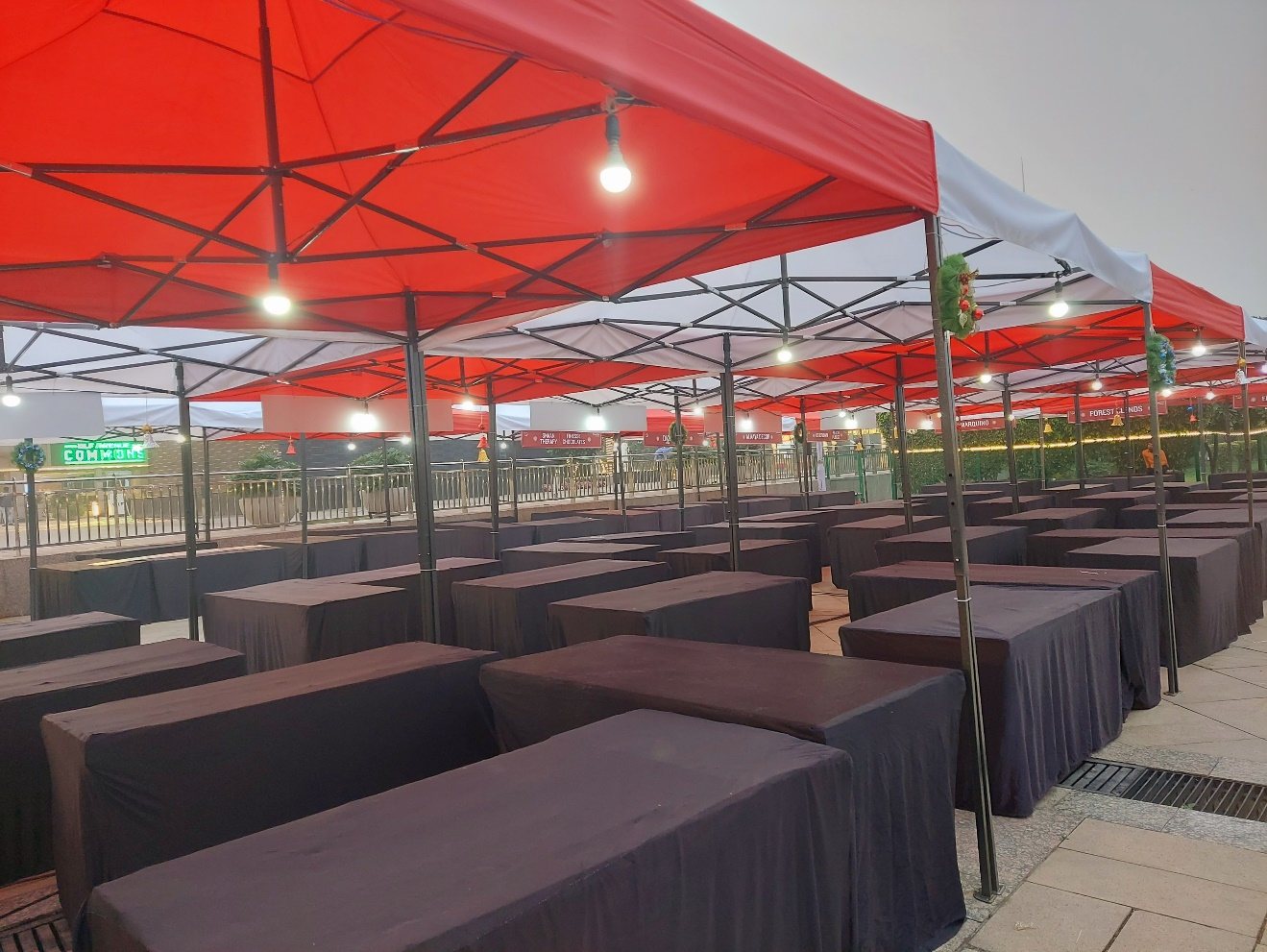 Long rows of dark lounge seating under red canopies at an outdoor event