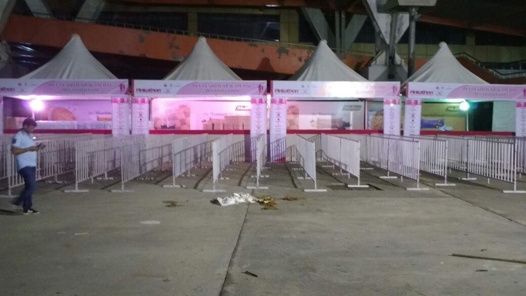 Row of pagoda tents lit in pink behind metal crowd barricades at night